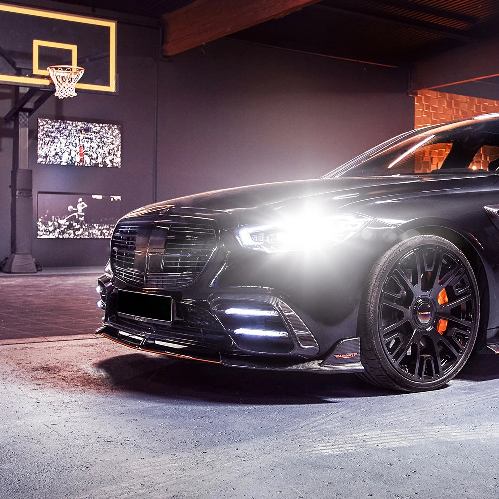 A black car with bright LED headlights is displayed in a dark studio setting.