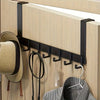 A black over-the-door coat rack with six hooks mounted on a light wood panel, holding a hat and a striped garment.
