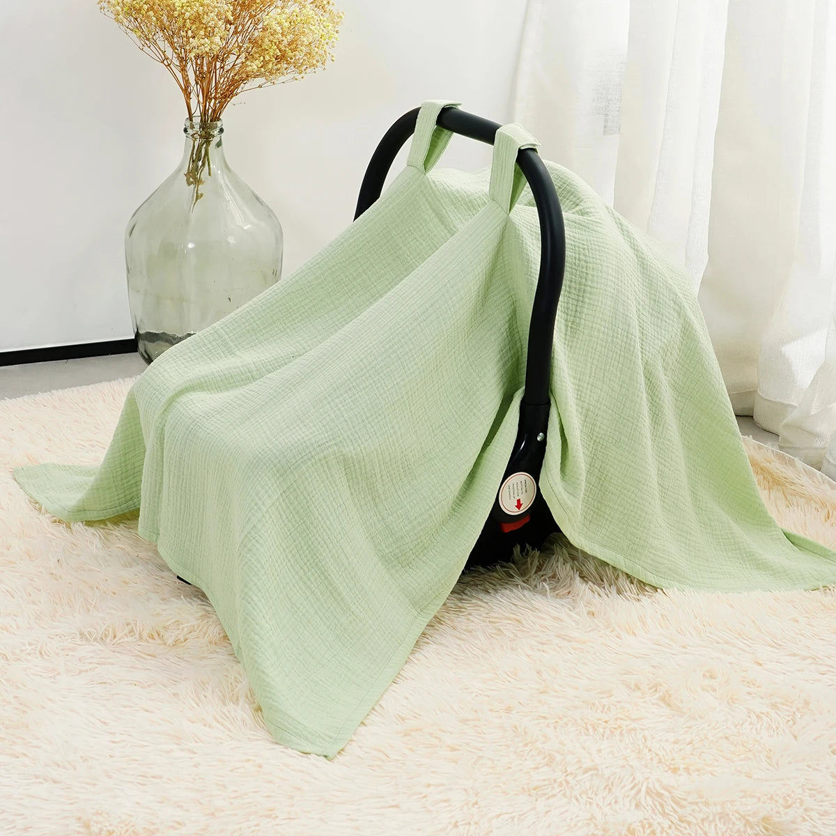 A light green breathable cotton muslin car seat and stroller cover draped on a fluffy rug.