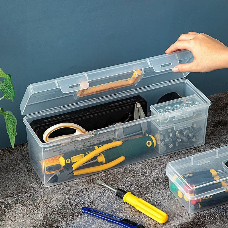 A clear multi-compartment tool organizer box filled with various hand tools and accessories on a dark surface.