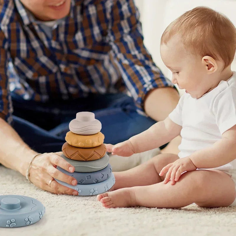 A baby is interacting with a stack of soft silicone building blocks on a light surface.
