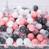 A white plastic basket filled with a large quantity of colorful clear and opaque ball pit balls in pink, white, and black.
