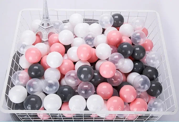 A white plastic basket filled with a large quantity of colorful clear and opaque ball pit balls in pink, white, and black.