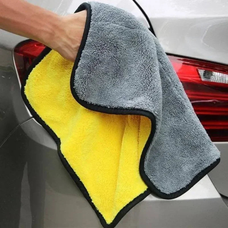 A hand is holding a yellow and gray microfiber cleaning towel against the rear of a car.