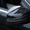 A close-up of a black car's rear window featuring a clear plastic rearview mirror with a rhinestone guard.