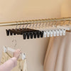 A close-up of a wooden hanger rack with adjustable clip hangers for clothing, showing black and white hangers.