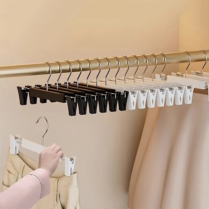 A close-up of a wooden hanger rack with adjustable clip hangers for clothing, showing black and white hangers.