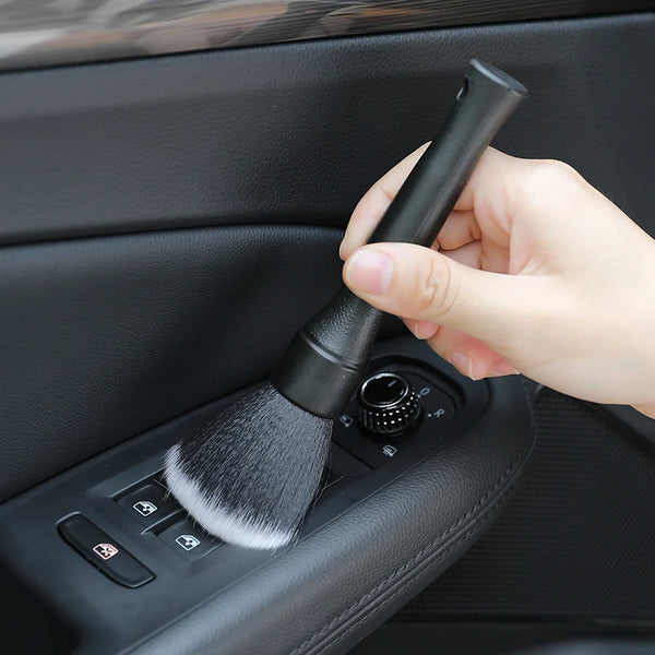 A hand is holding an ultra-soft detailing brush with a black handle, positioned over a car interior cleaning device.