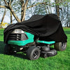 A teal heavy-duty yard tractor is shown with a black waterproof cover placed over it in a grassy field.