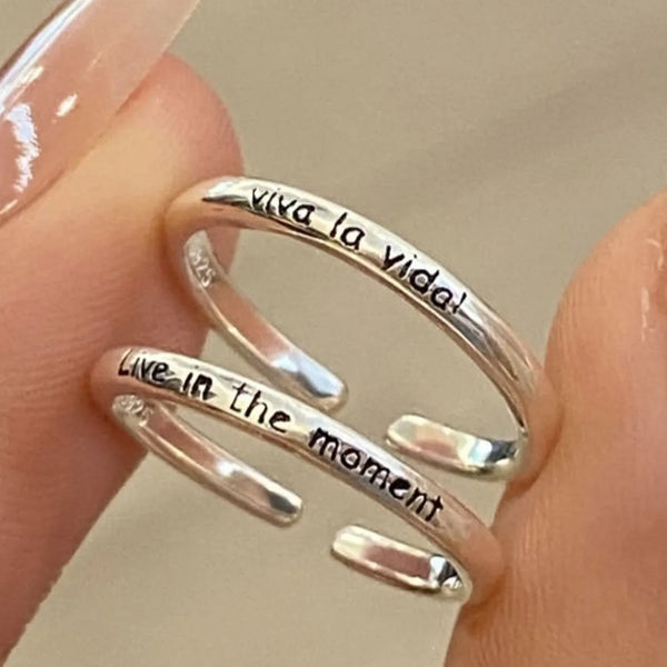 Nahaufnahme von drei verstellbaren Silber-Briefringen mit eingraviertem Text auf dem Finger einer Person.