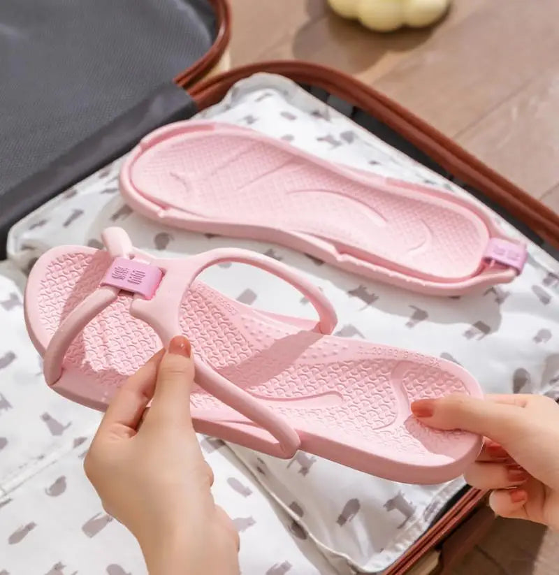 A pair of pink foldable EVA travel slippers being held by a person on a white cloth.