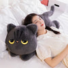 A woman is resting her head on a soft black cat plush toy while lying in white bedding.