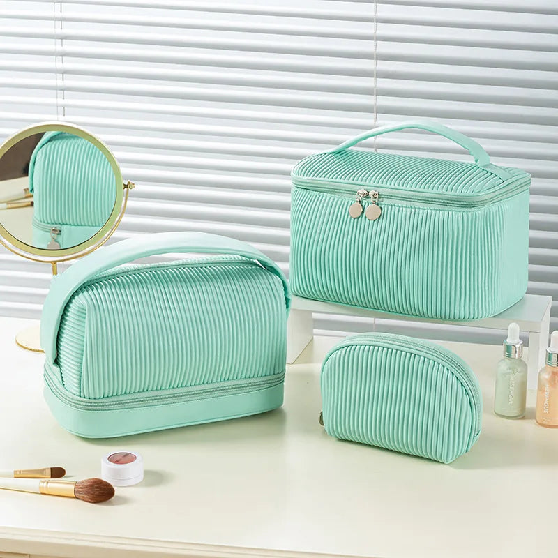A set of three mint green ribbed PU leather makeup bags displayed on a white surface next to a mirror.