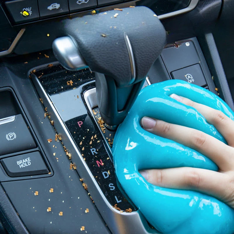 A hand is squeezing a bright blue reusable cleaning gel for car interiors and hard-to-reach gaps.
