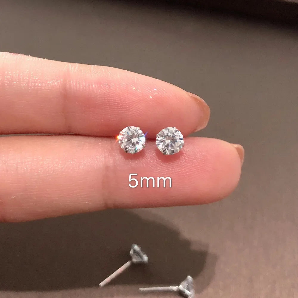 Une main tient de minuscules clous d'oreilles en cristal CZ transparent, mesurant 5 mm, sur un doigt.