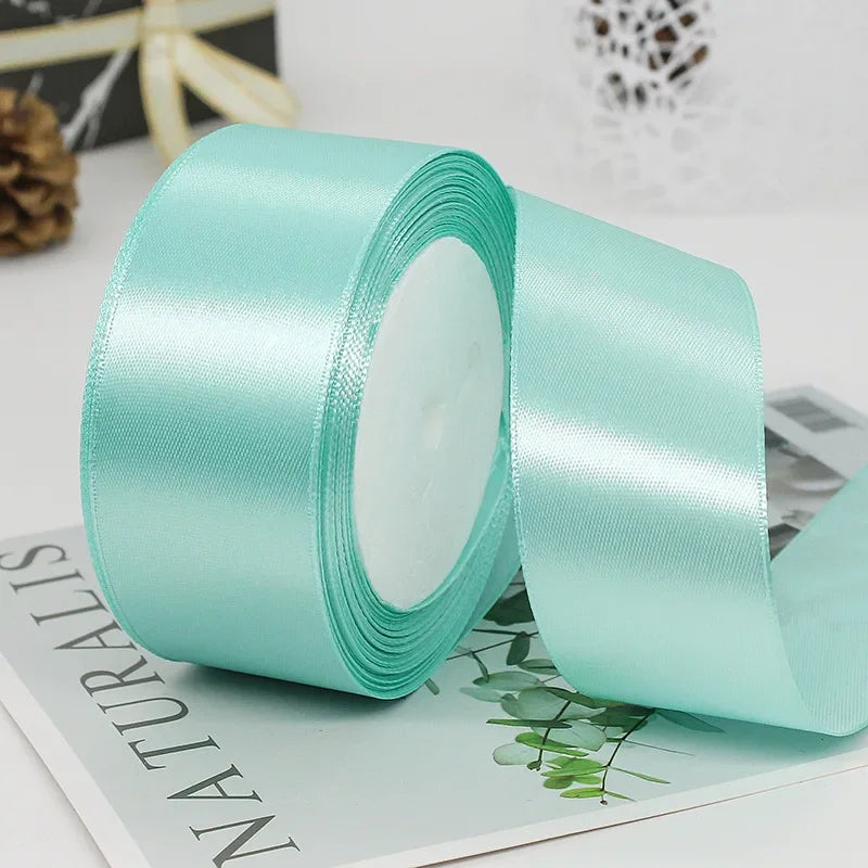 A roll of mint green satin ribbon used for gift wrapping and DIY crafts.