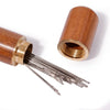 A set of self-threading sewing needles with a wooden storage cylinder.