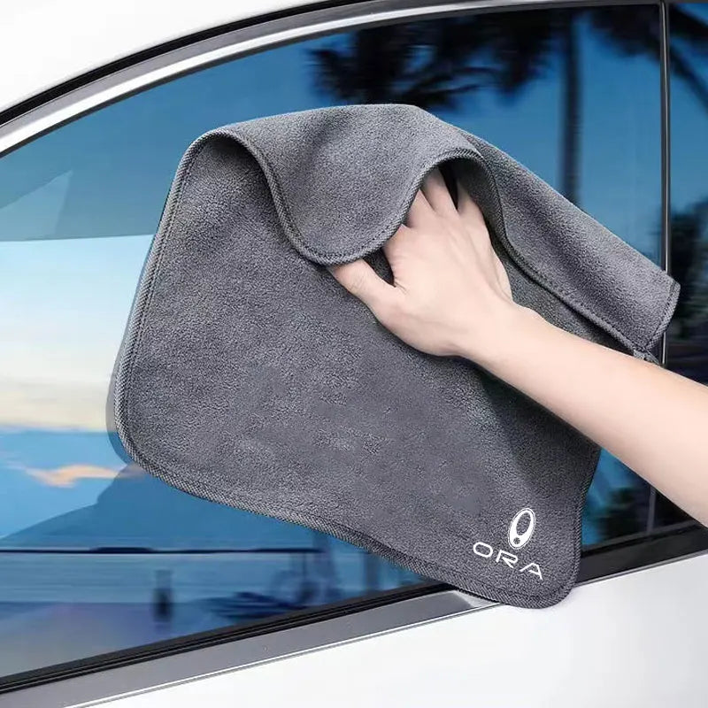 A hand is holding a gray ultra-soft coral fleece car drying towel against a glass window.