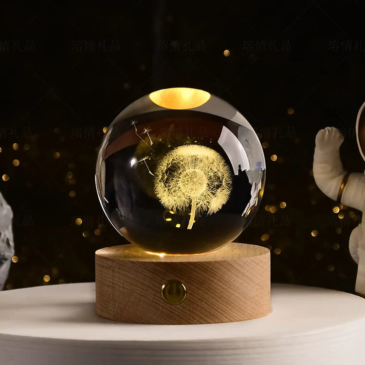 A laser engraved crystal ball night light with a golden glow resting on a wooden base.