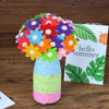 A colorful bouquet of felt flowers and buttons arranged in a cylindrical vase on a wooden surface.