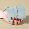 A hand holds a light mint green PU leather wallet with a double-zip closure and card slots.