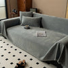 A gray chenille sofa throw draped over a sofa, featuring tassel edges and displayed on a light patterned rug.