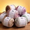 A pile of three spools of MuYuan Frost Words glitter yarn in various shades of pink and green on a wooden surface.