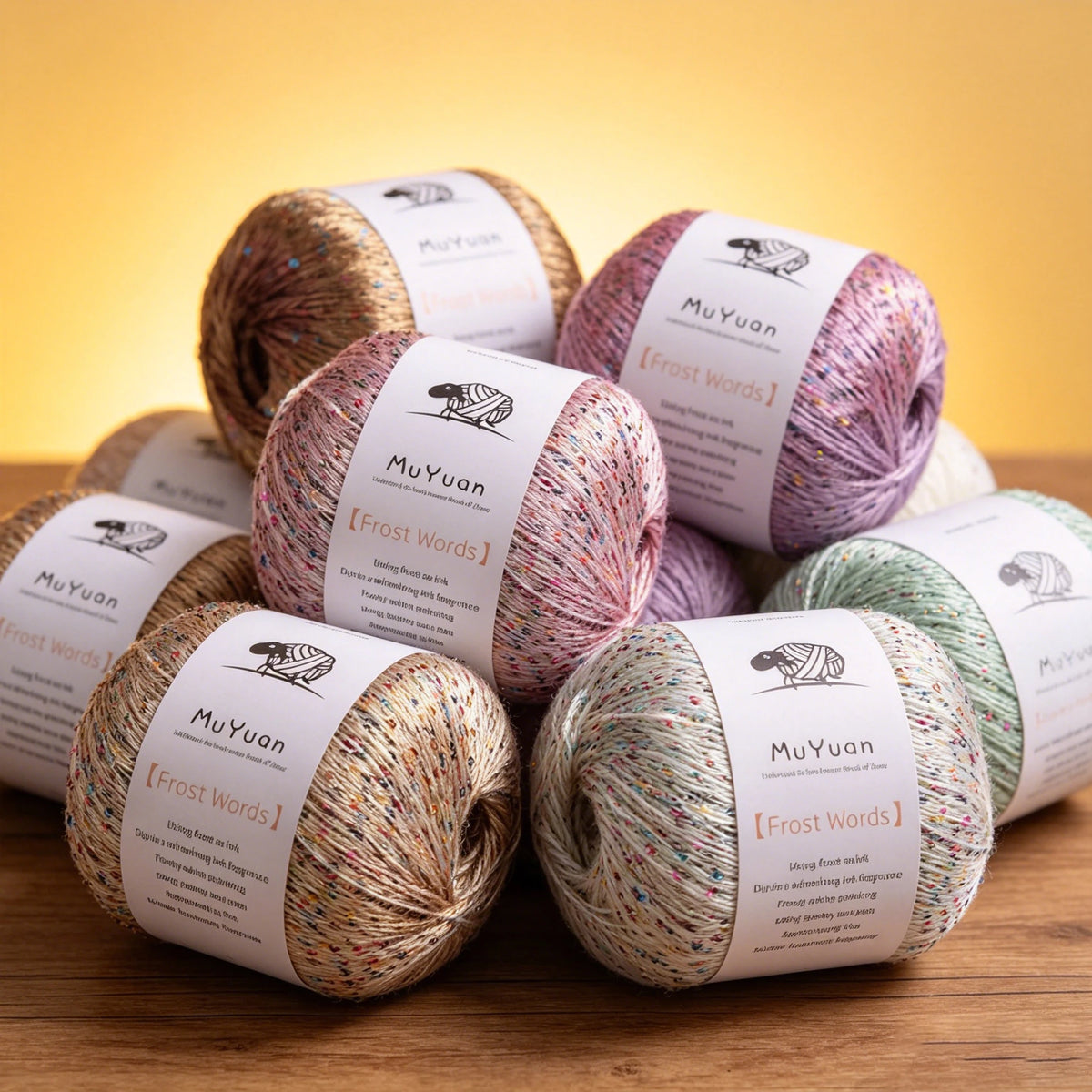 A pile of three spools of MuYuan Frost Words glitter yarn in various shades of pink and green on a wooden surface.
