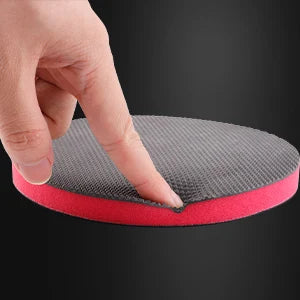 A hand is pressing a reusable magic clay pad for paint detailing, showing the textured gray and red surfaces.