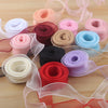 A collection of rolled satin ribbon in various shades of pink, red, purple, and blue on a wooden surface.