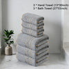 A stack of gray hand and bath towels with gold accents placed on a white marble floor.