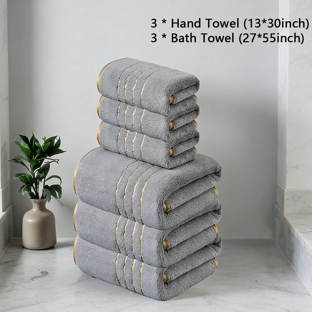 A stack of gray hand and bath towels with gold accents placed on a white marble floor.