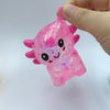 A hand holds a pink, glittery axolotl squishy stress ball with an air vent.