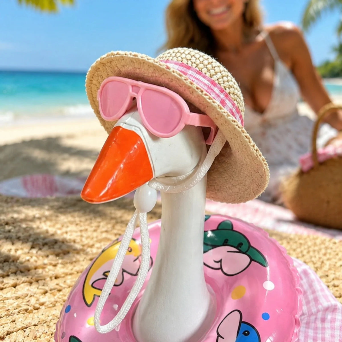 A pink plastic goose toy wearing sunglasses and a straw hat is placed on a sandy beach.