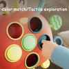 A close-up of a round, multi-colored silicone sensory toy with various openings and textures being explored by a hand.