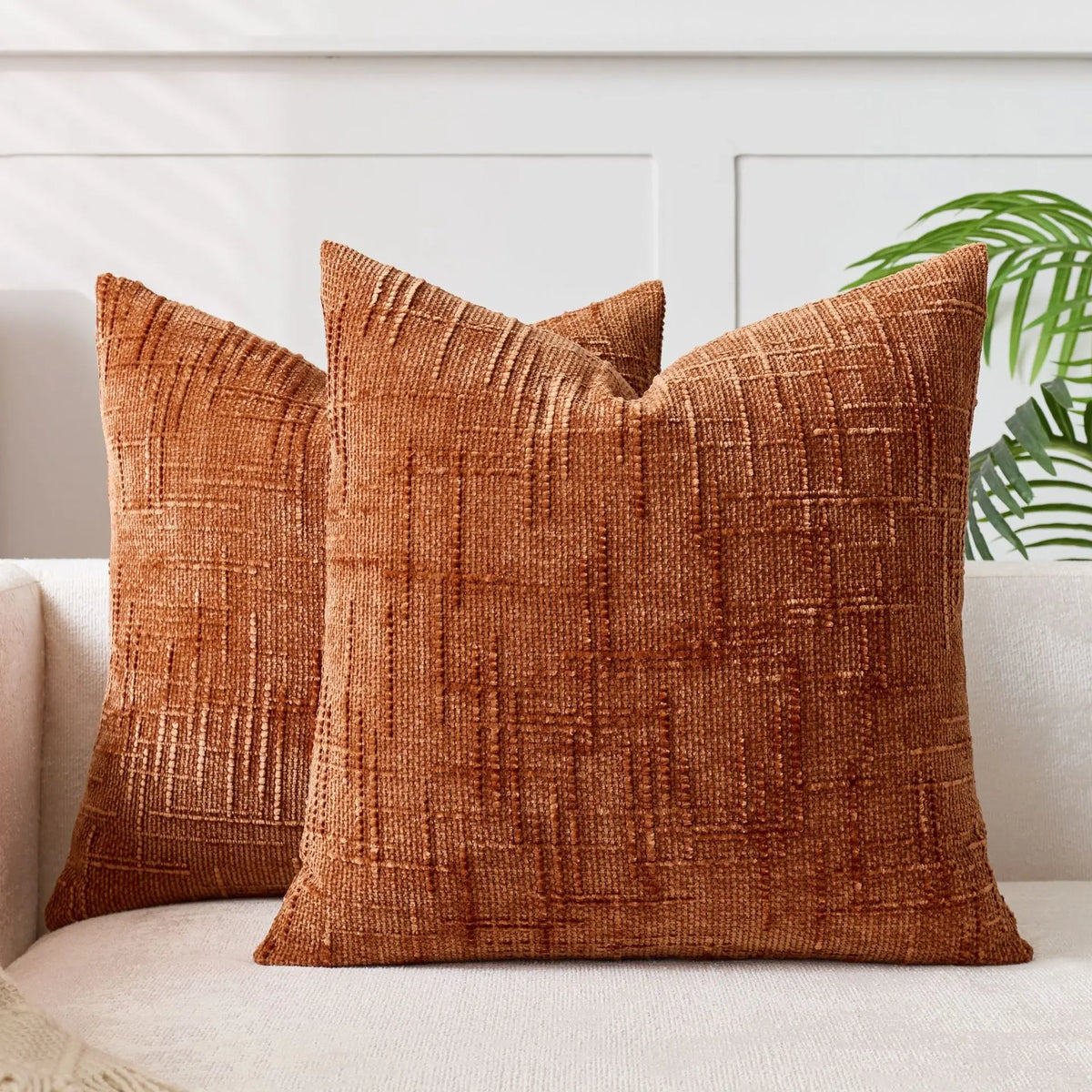 A square, rust-colored handwoven chenille texture cushion cover resting on a light sofa.