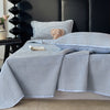 A light blue and white checkered quilted bedspread with a fluffy teddy bear pillow on a dark headboard.