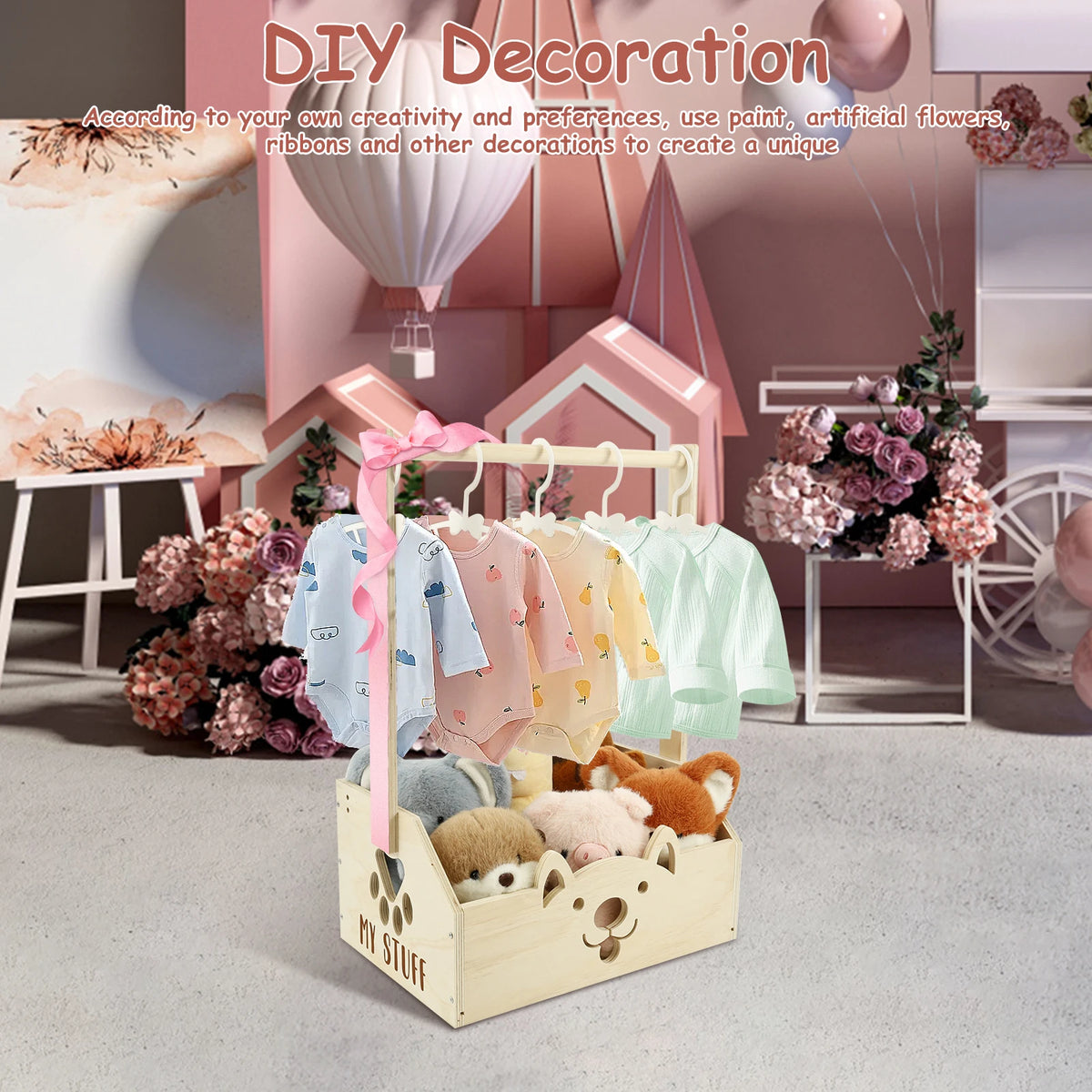 A wooden storage crate with a handle is filled with baby essentials and toys, set in a pink decorative scene.