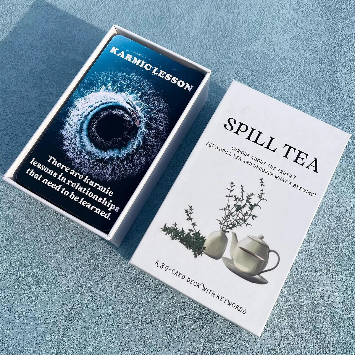 A box of the Spill Tea Oracle Card Deck with a title card for Karmic Lesson