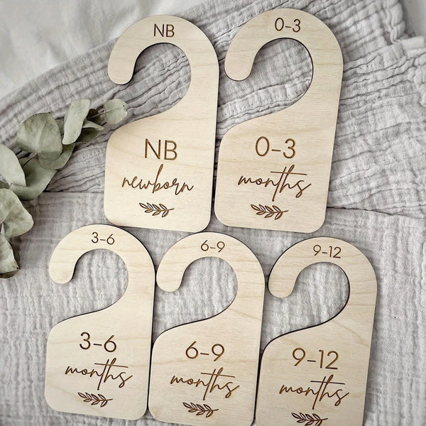 A set of seven wooden baby closet divider hangers marked with age ranges from newborn to 9-12 months