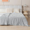 A light gray brushed flannel throw blanket draped over a bed with white pillows and a bedside lamp.