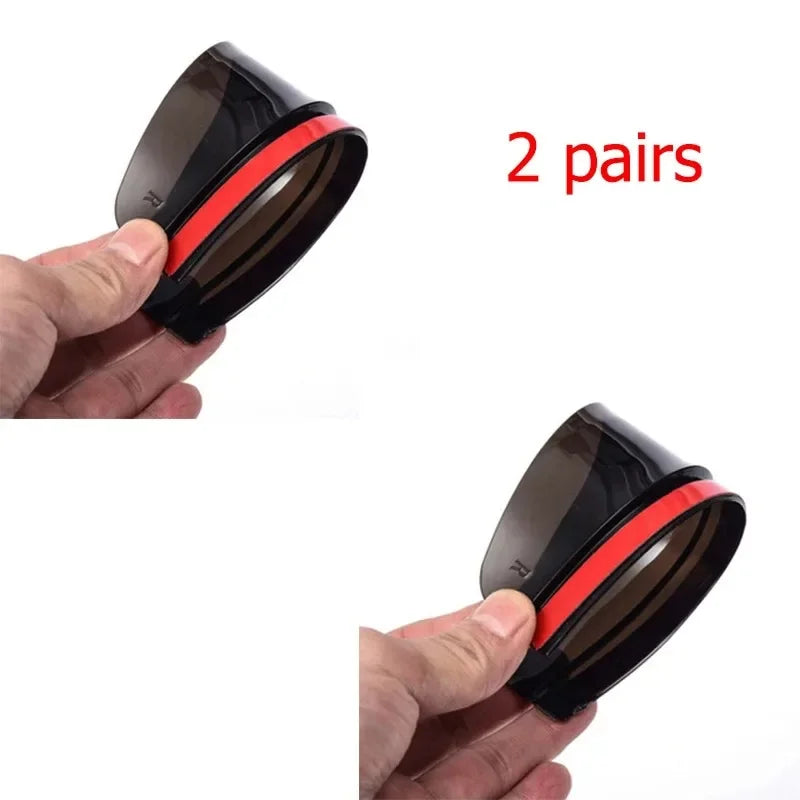 Two pairs of black and red carbon fiber car side mirror rain and sun visors being held by a hand.
