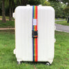 A white suitcase with colorful adjustable straps is placed on green grass next to a paved path.