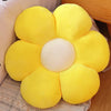 A bright yellow sunflower plush pillow with a white center, resting on a textured fabric.
