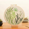 A circular embroidery hoop featuring floral cross stitch designs on a beige fabric, displayed on a wooden stand.