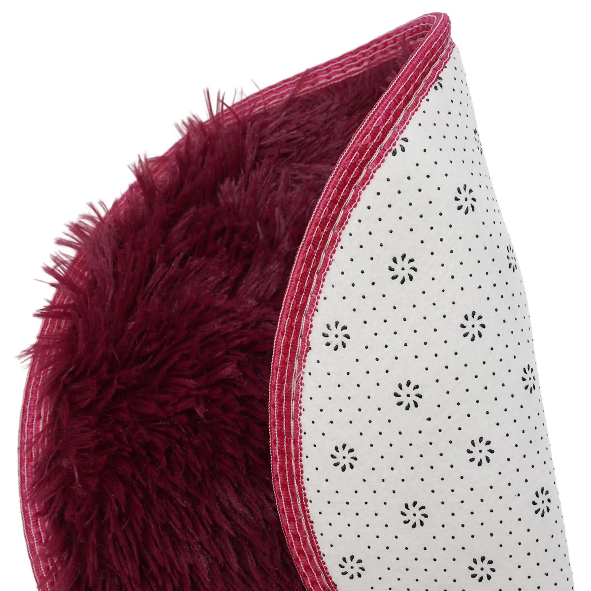 A close-up of a deep burgundy shaggy round rug with white polka dots and red trim.
