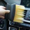 A hand holds a black detailing brush set with soft yellow bristles, positioned near a car interior panel.