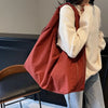 A person is holding a reddish-brown nylon tote bag with a zipper closure against a dark background.