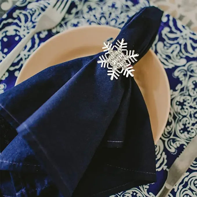 A dark blue satin napkin tied with a silver snowflake ring on a light pink plate set on a blue patterned cloth.