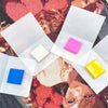 A collection of pink and yellow silicone diamond painting clay pieces are displayed on a patterned fabric.